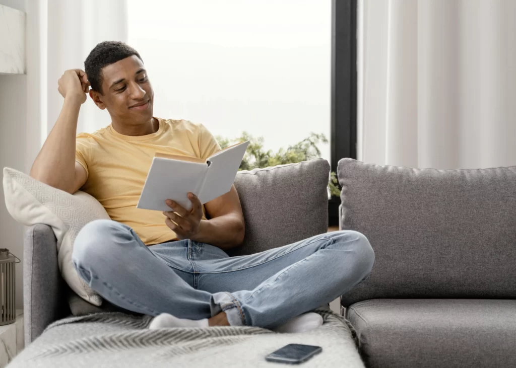 Homem sorrindo e relaxando no sofá enquanto lê um livro